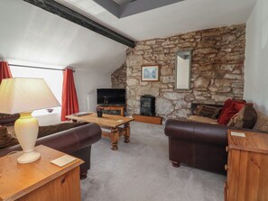 Ein gemütliches Wohnzimmer mit Steinwand, Kamin, Fernseher und Ledersofas.
