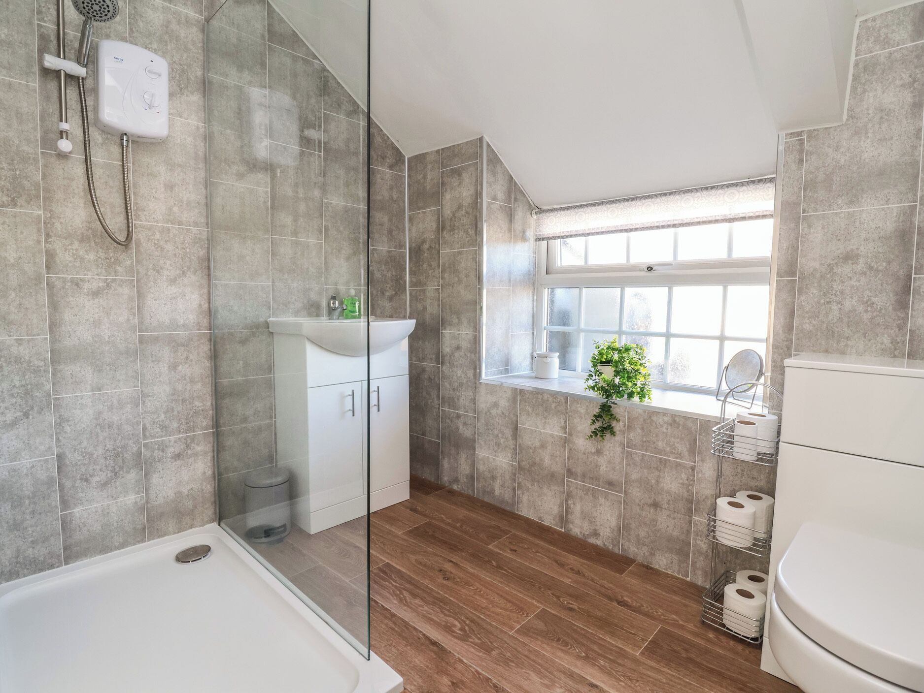 A modern bathroom with a glass shower enclosure, a white sink, a window with a view, and a toilet.