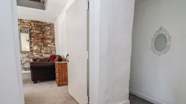 A hallway with a stone wall, a wooden cabinet, a brown leather sofa, and a white door. - Upstairs at the Sun Inn (Mold)