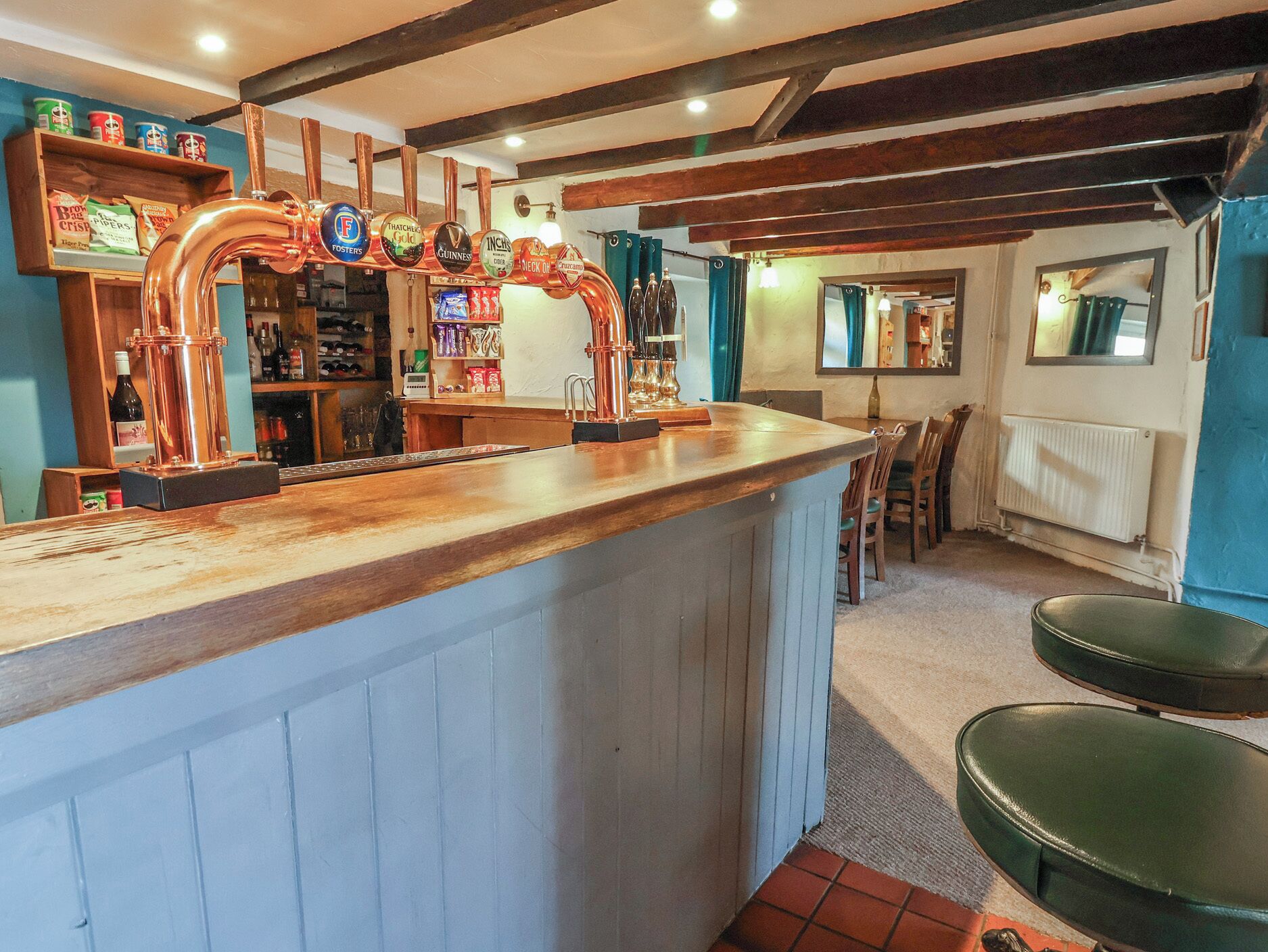 A bar area with copper beer taps, shelves with bottles, and a wooden counter.
