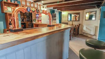 Una zona de bar con grifos de cerveza de cobre, estantes con botellas y una barra de madera.