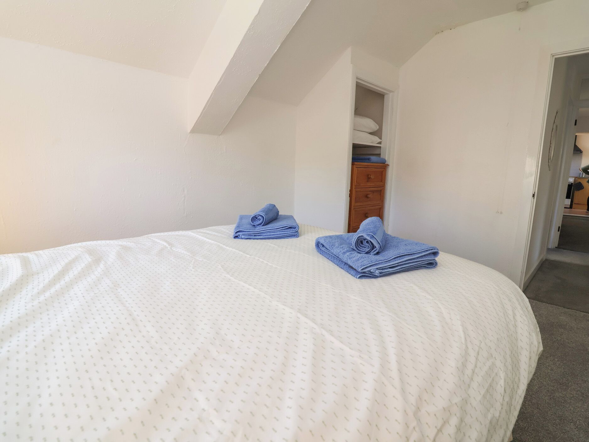 A bedroom with a bed, two blue towels, a wooden dresser, and a white door leading to another room.