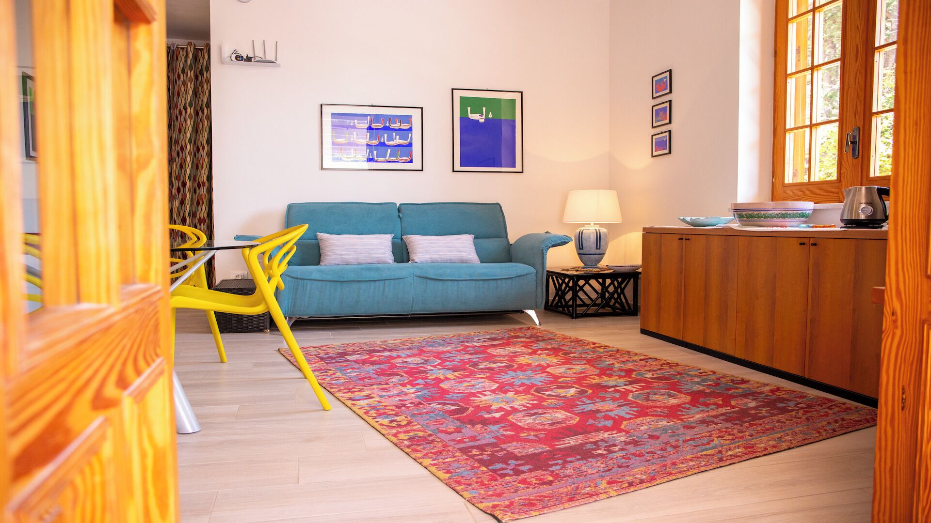 A living room with a blue sofa, yellow chair, patterned rug, and wooden cabinets.
