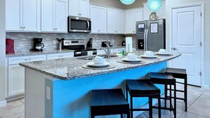 A modern kitchen with white cabinets, stainless steel appliances, a granite countertop, and blue pendant lights. - South-Facing Pool & Spa • Lazy River & Waterslides • Gated Resort • Near Disney (Davenport)