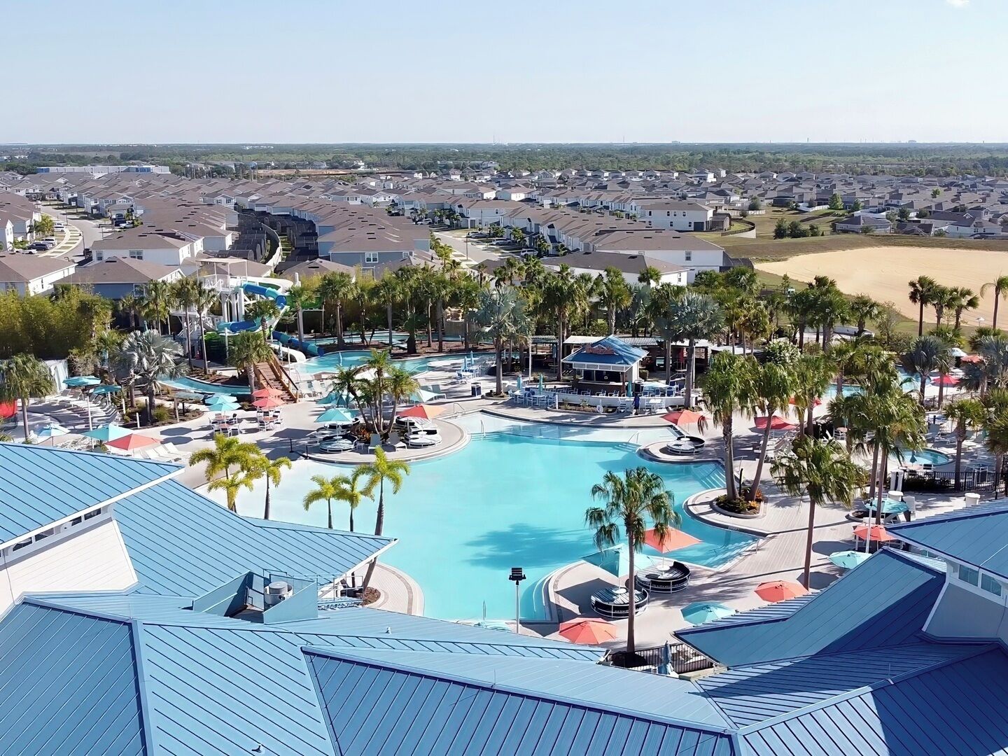 A resort with a large pool, palm trees, and a view of the surrounding neighborhood.