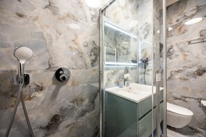 A modern bathroom with a glass-enclosed shower, a marble wall, and a white toilet.