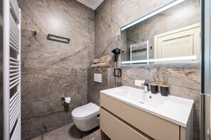 A bathroom with a marble wall, a white sink, a towel rack, and a toilet.