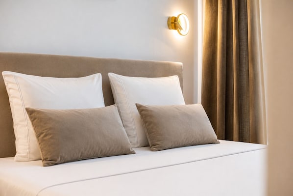 A bed with white and beige pillows, a beige headboard, and a wall-mounted light fixture.