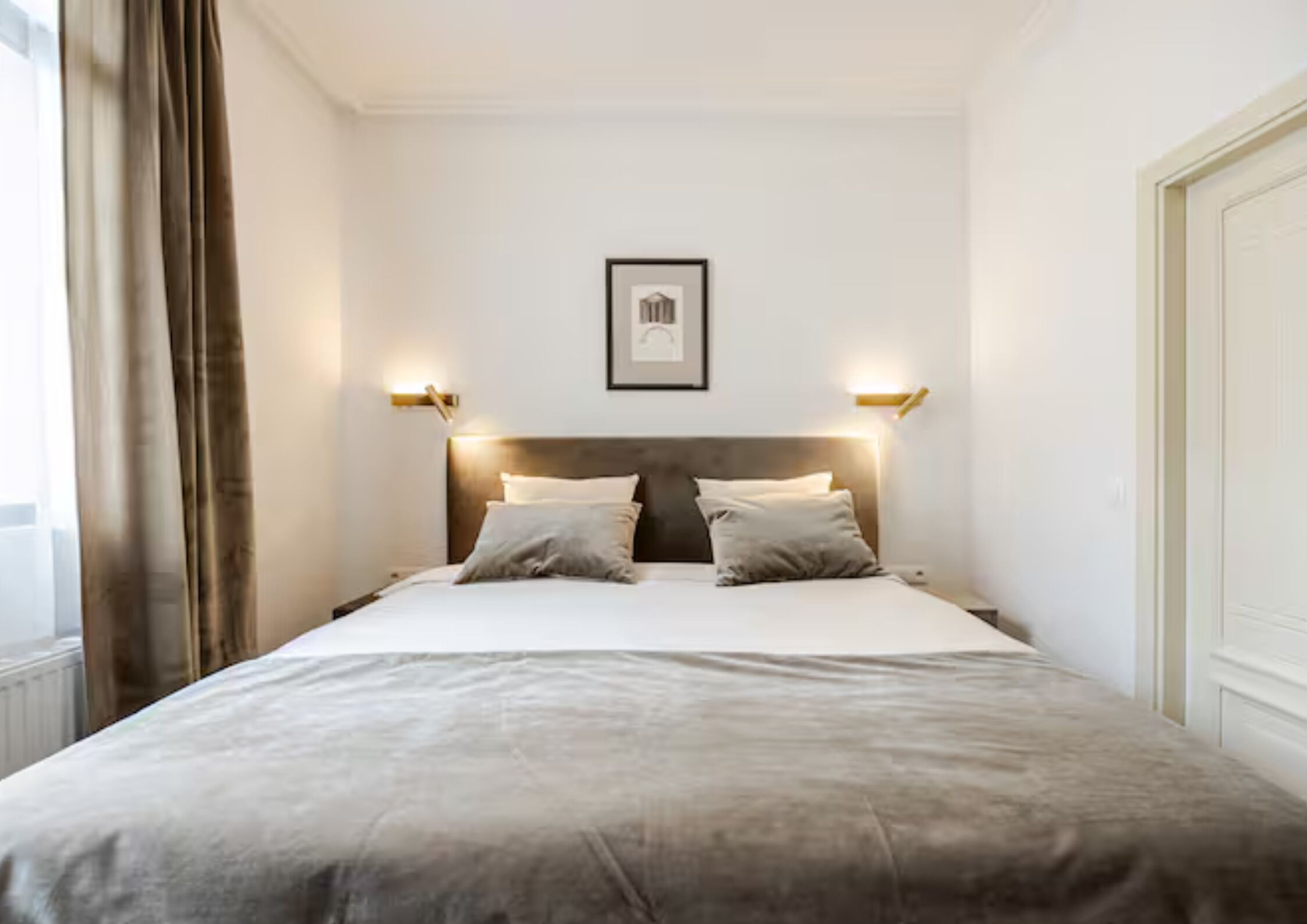 Una camera d'albergo con un letto, due comodini, una testiera, un quadro appeso alla parete e una finestra con tende.