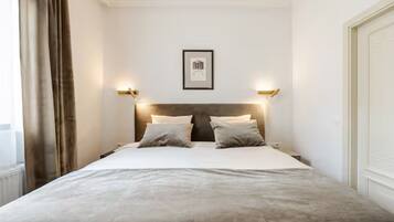 Una camera d'albergo con un letto, due comodini, una testiera, un quadro appeso alla parete e una finestra con tende.