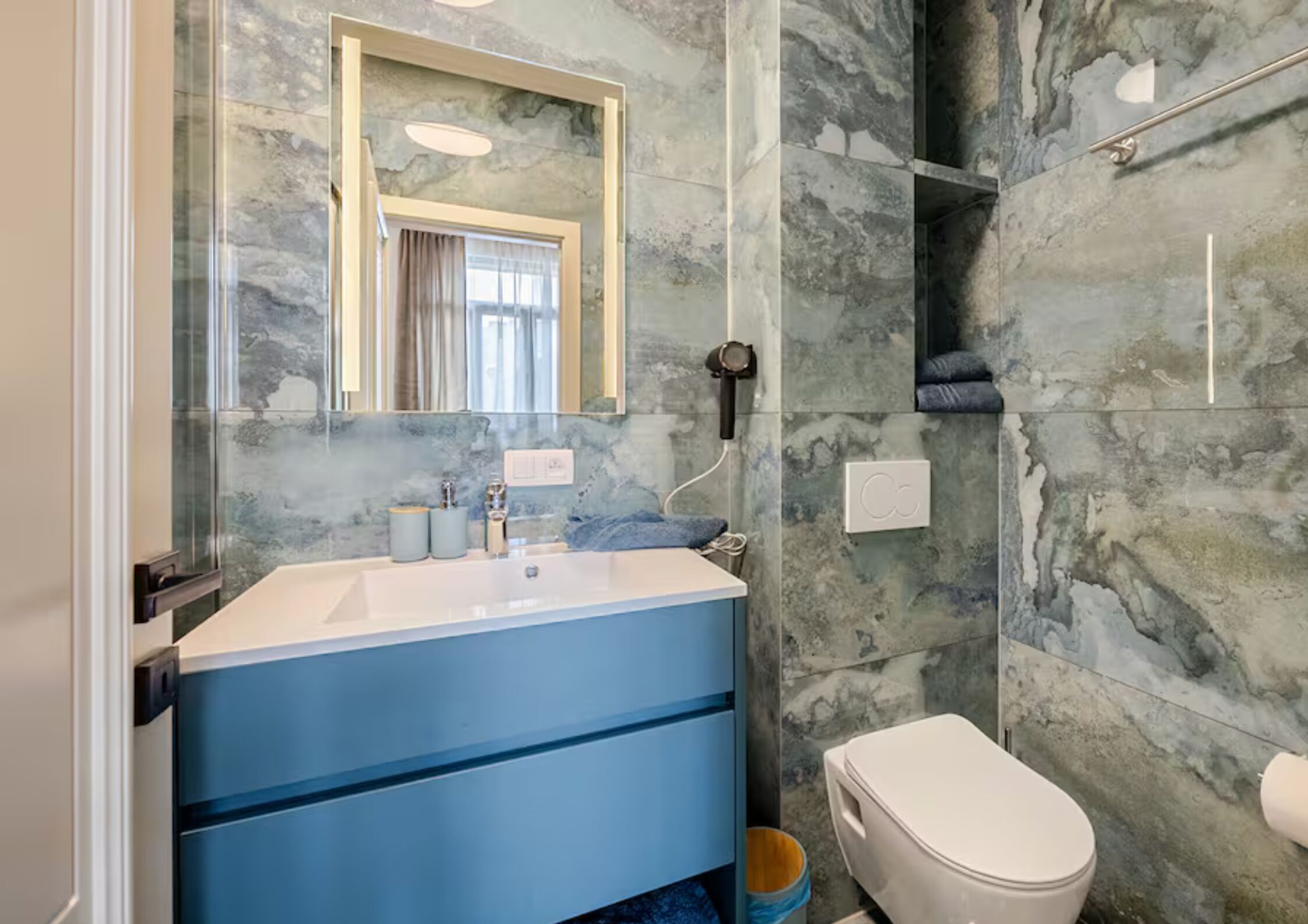 Une salle de bain avec un mur en marbre, un lavabo, un miroir, des toilettes et une douche.