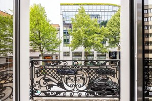A balcony with ornate metal railings, a view of a modern building with glass windows, and trees in the background. - Gemstay (Antwerp)