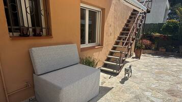 Un patio de piedra con un sofá, una ventana con rejas, una escalera y un perro pequeño.