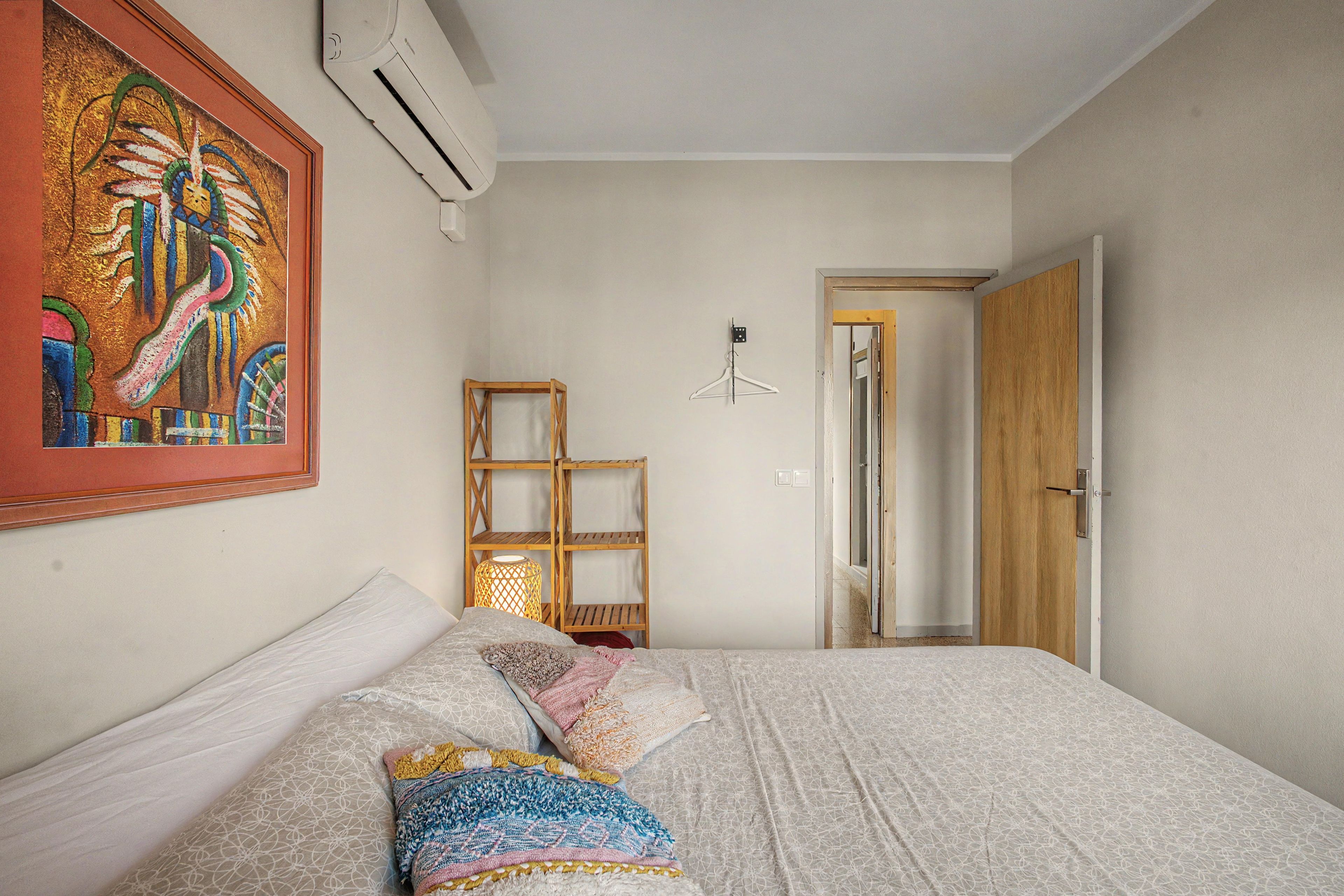 Une chambre à coucher avec un lit, une lampe suspendue, une étagère en bois et une porte.