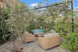 An outdoor patio with wicker furniture, a glass table, and a pergola covered with climbing plants.
