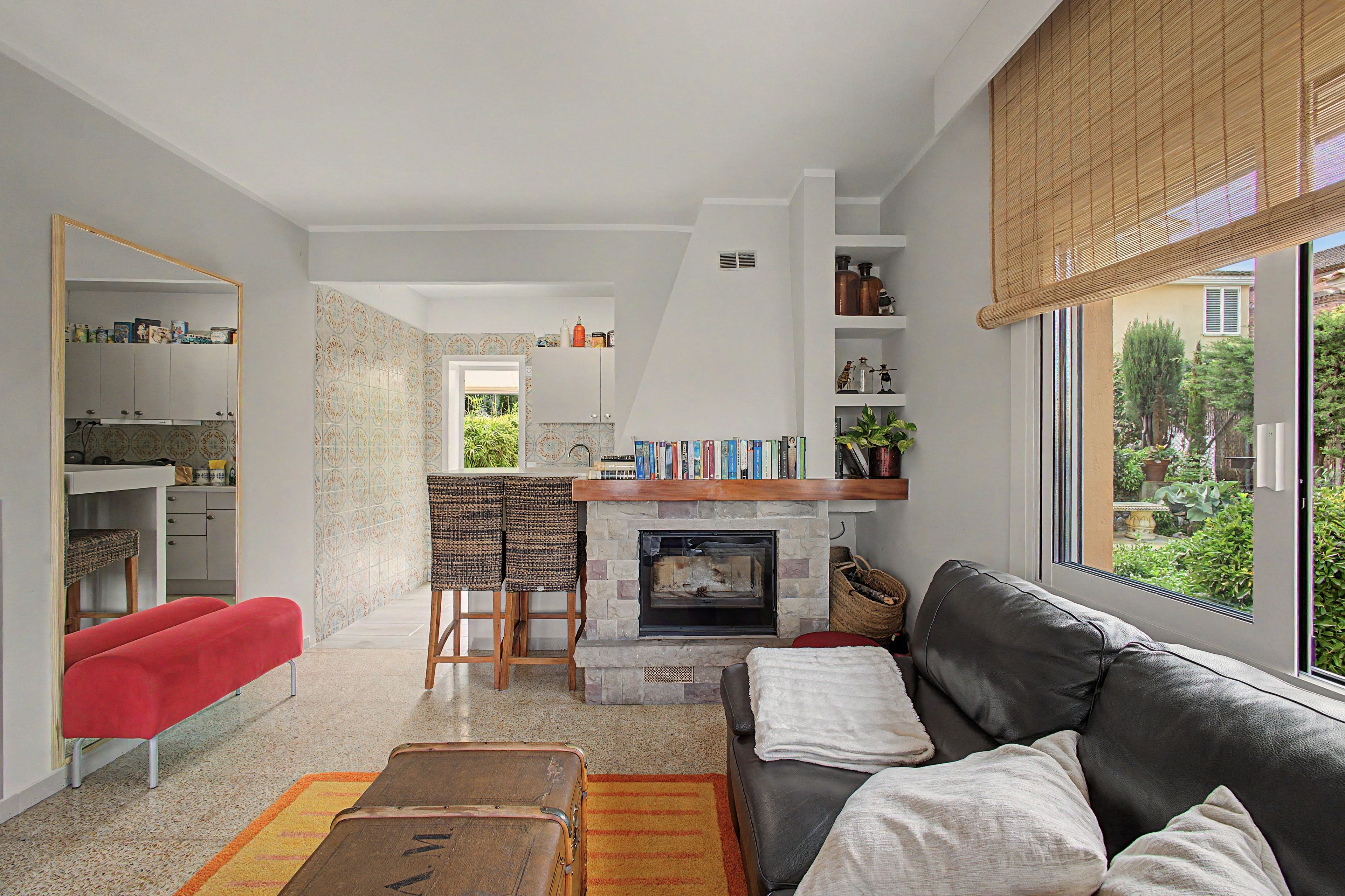 Een woonkamer met een open haard, een bank, een rode fauteuil, en een eethoek met een tafel en stoelen.