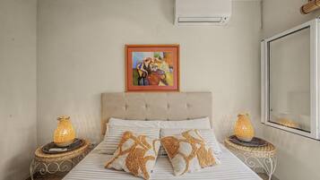 A bedroom with a bed, two nightstands, a wall-mounted air conditioner, and a framed painting.