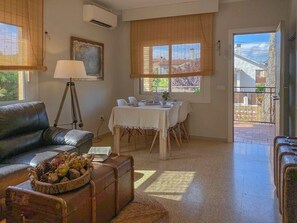 A living room with a leather sofa, a dining table with chairs, a lamp, and a painting on the wall. - Holiday Home 'California Relax Near Sitges' with Private Pool, Wi-Fi & Air Conditioning (Califòrnia)