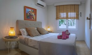 Un dormitorio con cama, dos lámparas de noche, una ventana con persianas, un cuadro en la pared y una puerta con manija.