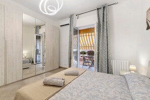 A modern bedroom with a large bed, a mirror, a wardrobe, and a view of the outside.