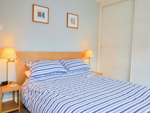 Ein Bett mit gestreifter Bettwäsche, zwei Nachttischlampen und zwei gerahmte Bilder an der Wand.