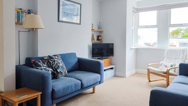 Ein Wohnzimmer mit einem blauen Sofa, einem Fernseher, einer Lampe und einem Fenster mit Blick.