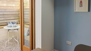 Ein Zimmer mit Holztür, einem kleinen Tisch mit einer Tablett voller Tassen und Untertassen, einem Stuhl und einem an der Wand befestigten Lichtschalter.