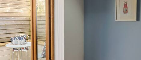 A room with a wooden door, a small table with a tray of cups and saucers, a chair, and a wall-mounted light switch.