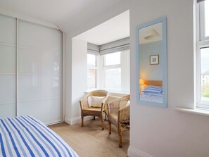 A bedroom with a bed, two wicker chairs, a window, and a mirror on the wall. - Peaslands (Sidmouth)