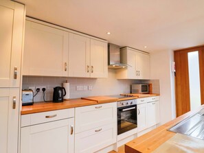 A modern kitchen with white cabinets, a wooden countertop, a built-in oven, and a microwave. - Peaslands (Sidmouth)