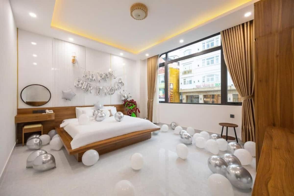 Quarto de hotel moderno com uma cama grande, cabeceira de madeira, mesa de cabeceira, espelho e vista da cidade através de grandes janelas.