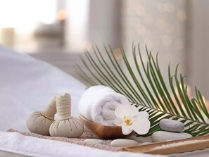 A spa setting with a massage table, a wooden bowl, a rolled-up towel, a massage ball, a white orchid, and a palm leaf. - Nelly Hotel - 200m to Dalat market (Xuan Huong - Da Lat)
