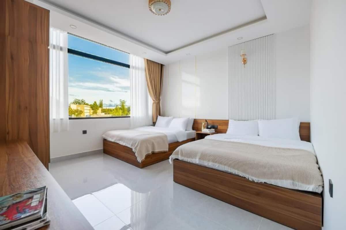 Quarto de hotel com duas camas, uma janela grande e vista para o verde.