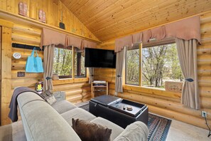 A log cabin interior with a sofa, a flat-screen TV, and a small table with a tray.