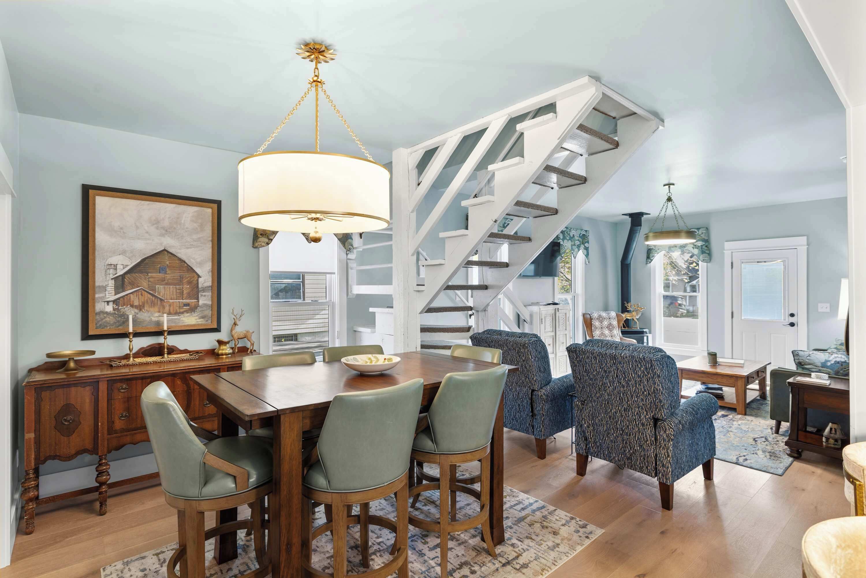 Un comedor con una mesa y sillas de madera, una escalera y un candelabro.