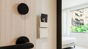 A modern room with a wooden door, a black handle, a white switch, and a black card with a gold design. - Hotel Ciencias Select (València)