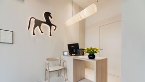 A reception desk with a computer, a chair, a wall-mounted horse silhouette, and a vase with flowers. - Hotel Ciencias Select (València)