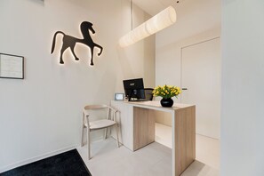 A reception desk with a computer, a chair, a wall-mounted horse silhouette, and a vase with flowers. - Hotel Ciencias Select (València)
