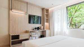 A modern hotel room with a bed, a desk with a chair, a TV, and a window with a view of trees. - Hotel Ciencias Select (València)