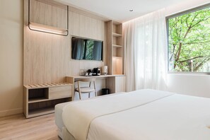 Una habitación de hotel moderna con una cama, un escritorio con silla, un televisor y una ventana con vistas a árboles.