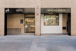 A hotel with a modern facade, featuring a horse logo and the name 'HOTEL' above the entrance. Adjacent to it is a store named 'CIENCIAS SELECT' with a large window display. - Hotel Ciencias Select (València)
