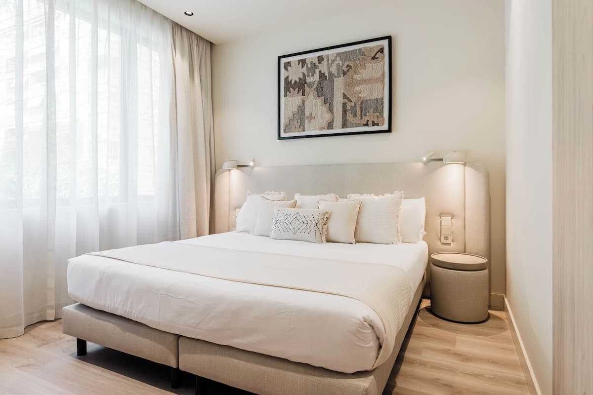 A neatly arranged bedroom with a large bed, bedside lamps, a small round table, and a framed artwork on the wall.