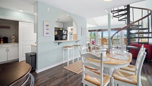 A modern kitchen with a central island, a dining area with a spiral staircase, and a view of the outdoors. - Spectacular Sunset Views, Quiet Location, Golf Cart Included, Private Deck - 7 Periwinkle Court (Fripp Island)