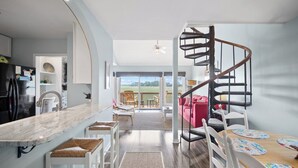 A modern kitchen with a marble countertop, white bar stools, and a spiral staircase leading to a balcony with a red sofa. - Spectacular Sunset Views, Quiet Location, Golf Cart Included, Private Deck - 7 Periwinkle Court (Fripp Island)