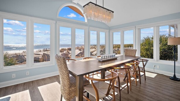 A spacious dining area with a view of the beach and ocean, large windows, and a chandelier. - Oceanfront, Private beach access, Golf Cart Included - 799 Marlin Drive (Fripp Island)
