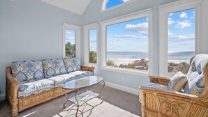 A room with a large window overlooking the ocean, a sofa, a chair, and a glass coffee table. - Oceanfront, Private beach access, Golf Cart Included - 799 Marlin Drive (Fripp Island)