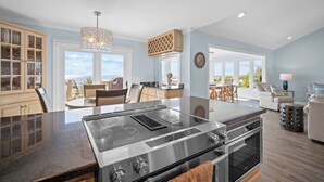 A modern kitchen with a central island, stainless steel appliances, and large windows offering views. - Oceanfront, Private beach access, Golf Cart Included - 799 Marlin Drive (Fripp Island)
