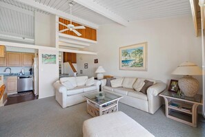 Ein geräumiger Wohnbereich mit einem weißen Sofa, einem Glastisch und einem Deckenventilator.