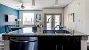 A modern kitchen with a granite countertop, stainless steel sink, and a ceiling fan. - Landing | Incredible 1BD, Courtyard, Gym (Manor)