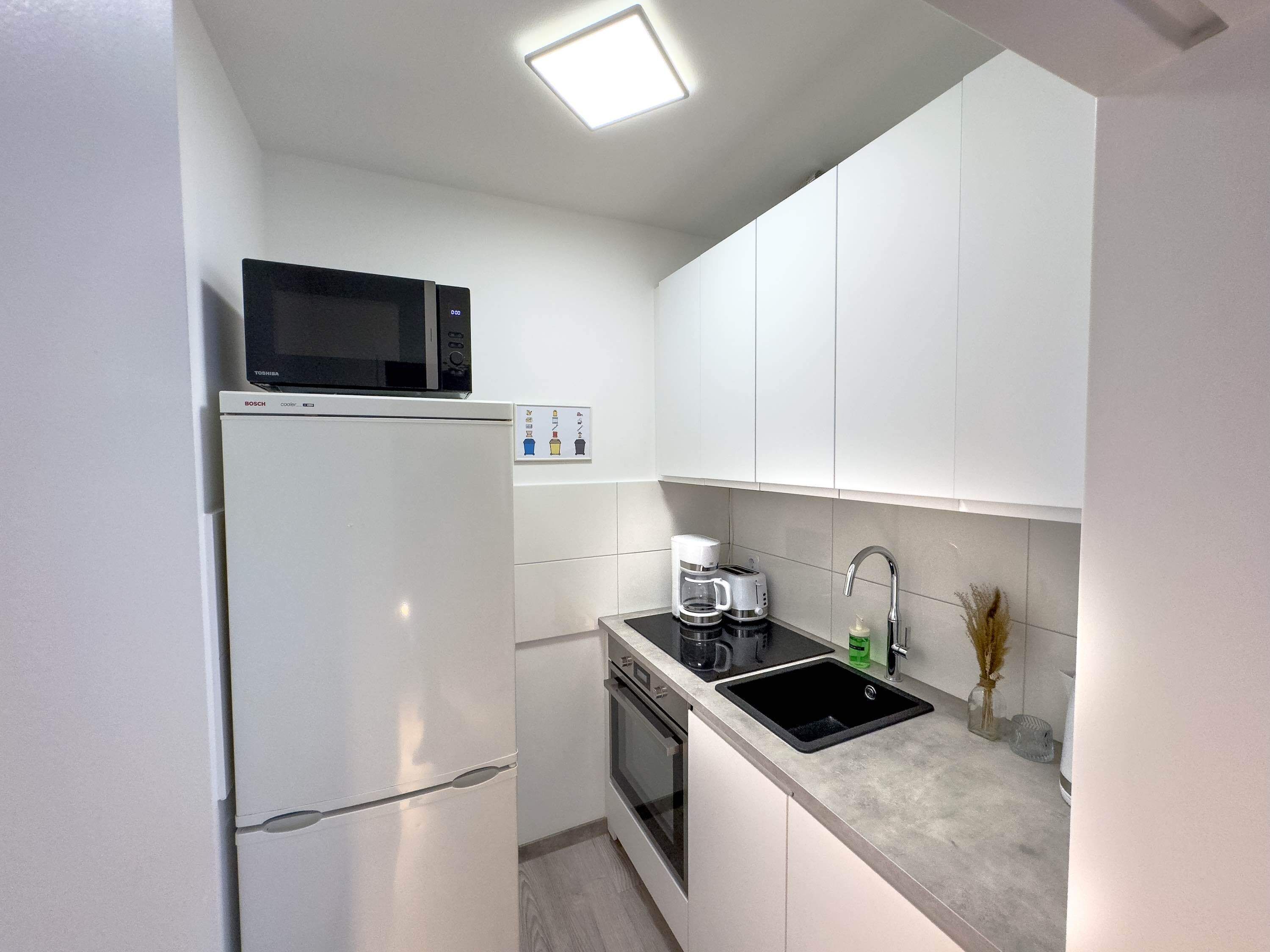 A compact kitchen with a refrigerator, microwave, coffee maker, and sink.